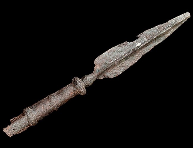 Corroded iron point and surviving metal shaft fittings of a captain’s staff against black.